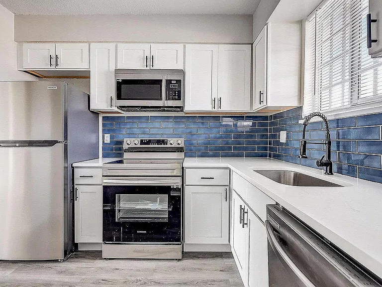 Modern kitchen with sleek stainless steel appliances, elegant white cabinetry, and striking blue subway tile backsplash.