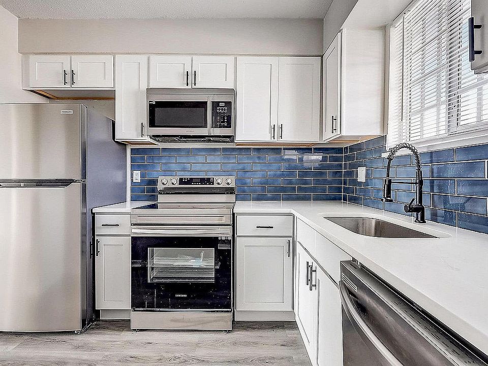Modern kitchen with sleek stainless steel appliances, elegant white cabinetry, and striking blue subway tile backsplash.