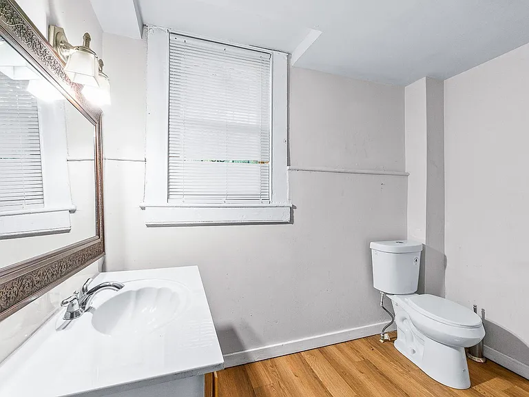 Compact bathroom with vanity sink, large framed mirror, and window with blinds for ventilation and natural light.