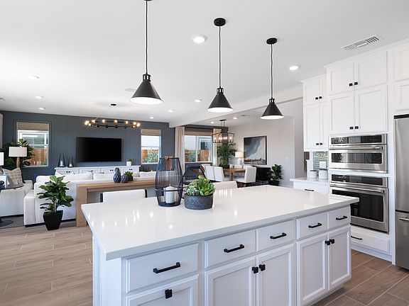 A modern, open-concept kitchen with a large white island, pendant lighting, and a mix of white and w