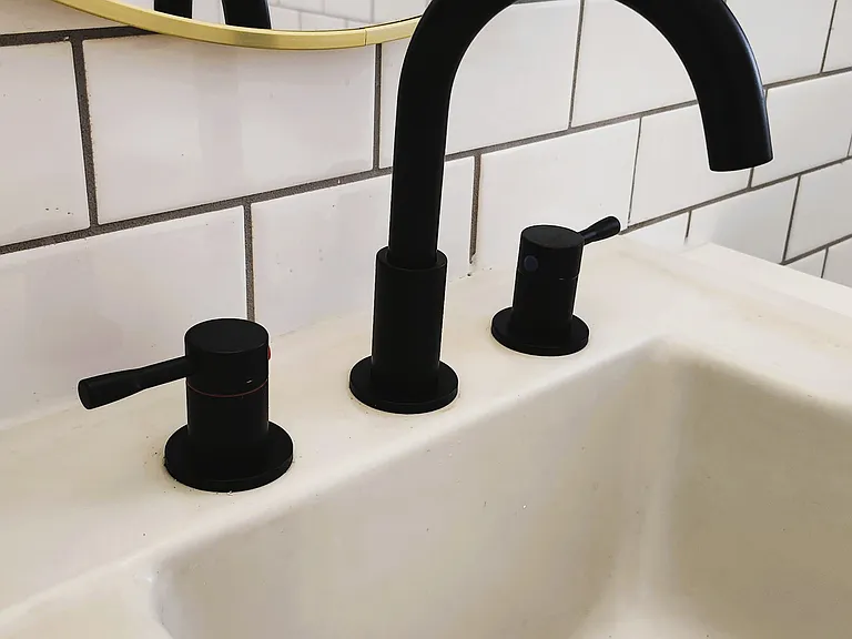 Sleek matte black faucet and handles, set against classic white subway tiles and a round mirror.