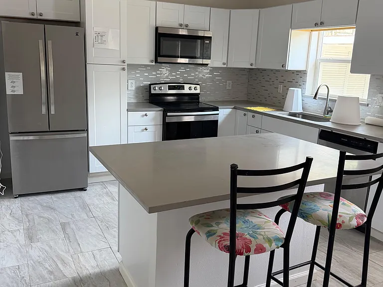U-shaped kitchen with stainless appliances, ample white cabinetry, tile backsplash, and a peninsula with bar seating.
