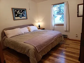 Upstairs hall bedroom, king bed, closet, ceiling fan with overhead light, window a/c, baseboard heater, hardwood floor.