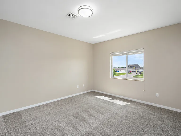 Bright and spacious primary bedroom with plush carpet, beige walls, large window, and ample natural light. Bright and spacious primary bedroom with plush carpet, beige walls, large window, and ample natural light.
