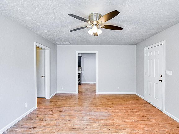 Living room with view of front door and entry to kitchen. Hallway to bedrooms on the left.