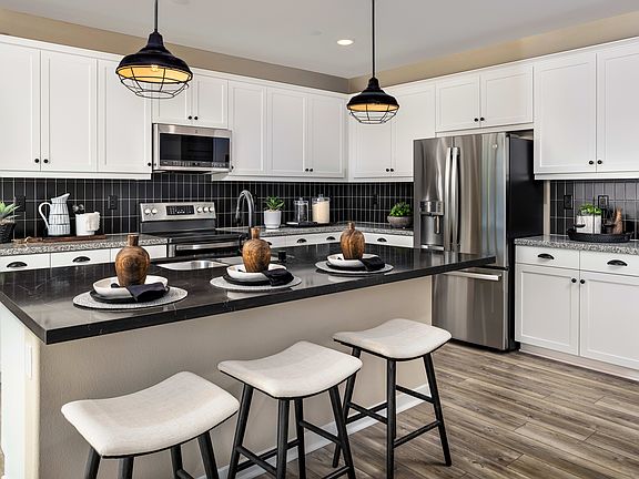 A modern and well-equipped kitchen with white cabinets, black countertops, and pendant lighting fixt