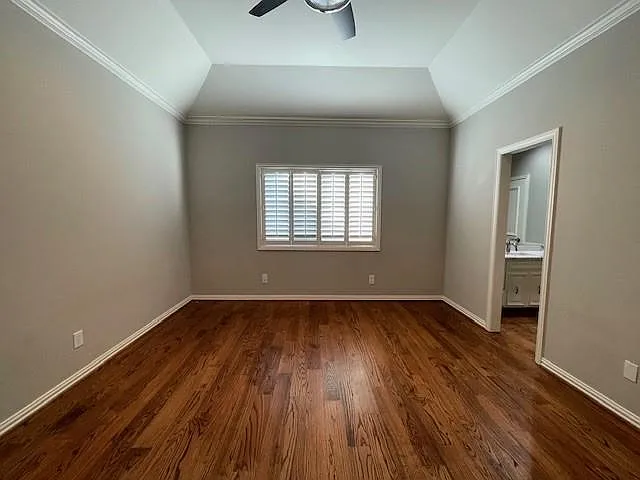 Unfurnished bedroom with ornamental molding, dark wood finished floors, vaulted ceiling, ceiling fan, and connected bathroom