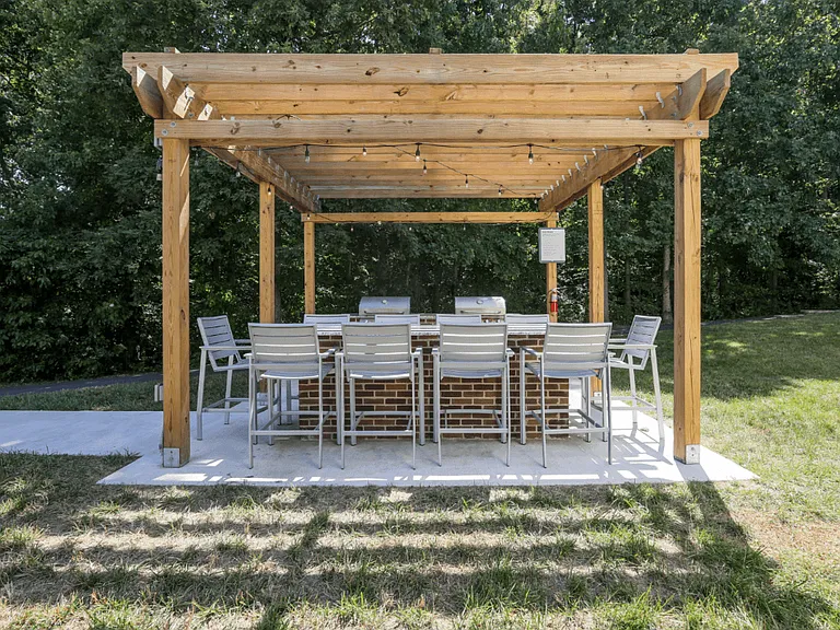 A wooden pergola with a large table and chairs by two BBQ grills at The Crossings at Russett in Laurel, MD