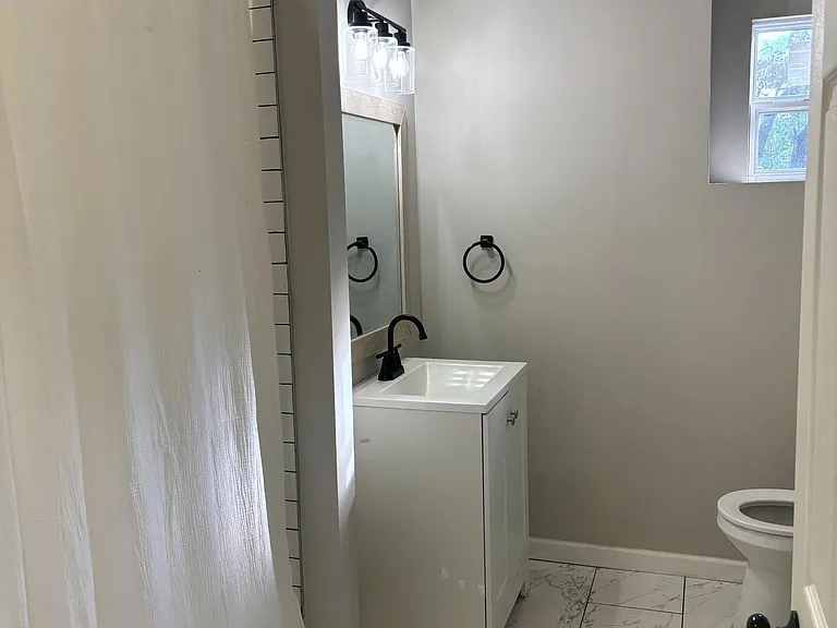 Updated full bathroom featuring a vanity with modern lighting, tiled shower, and easy-care tile flooring with window light.