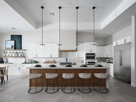 A modern, minimalist kitchen with white cabinets, a large central island with wooden stools, and pen