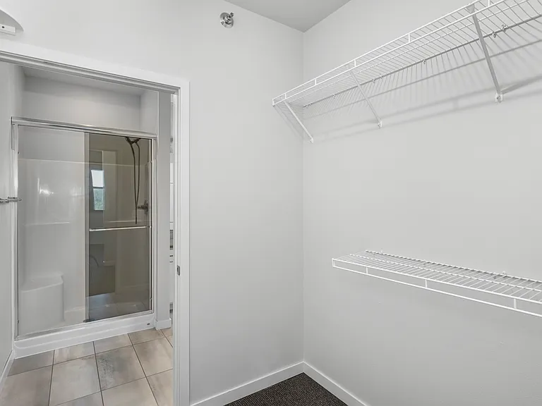 Chic walk-in closet with ample shelving space and a modern ensuite bathroom featuring a sleek glass shower. Chic walk-in closet with ample shelving space and a modern ensuite bathroom featuring a sleek glass shower.