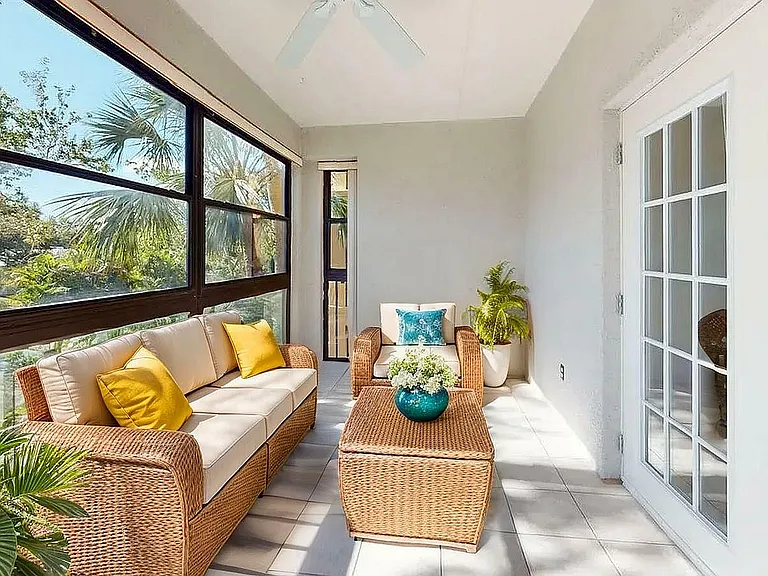 Inviting sunlit patio with chic wicker furniture, vibrant cushions, and lush greenery, ideal for relaxation amidst nature.