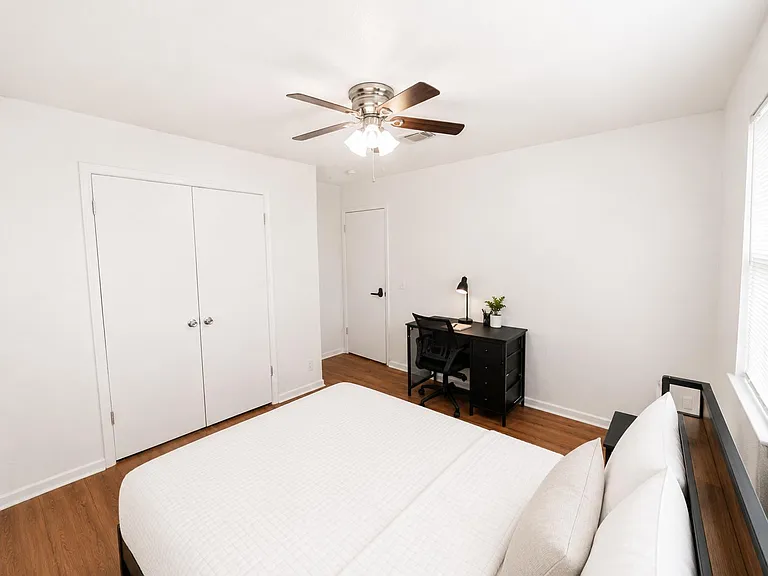 Bedroom with a ceiling fan, roomy closet, and a dedicated desk area, finished with wood-style flooring and a window for light