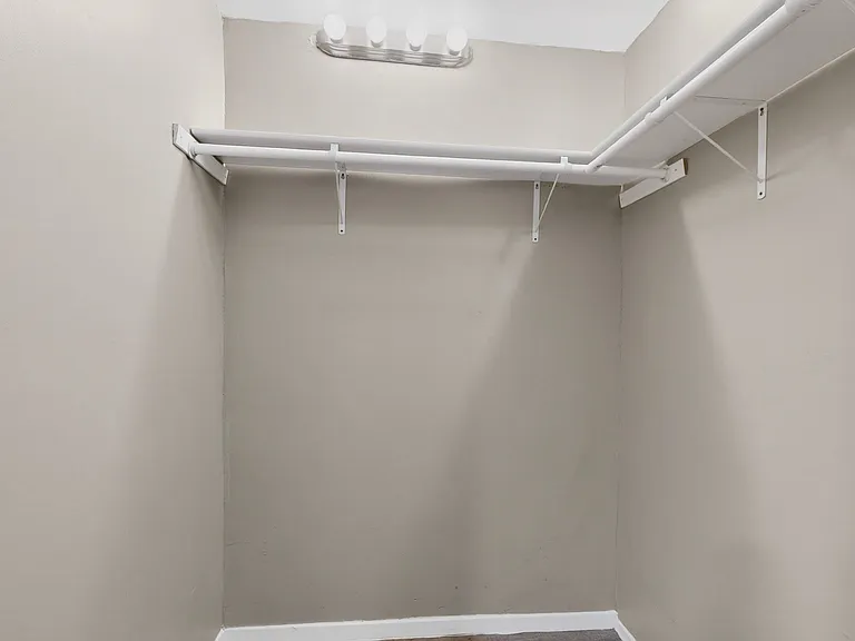 The primary bedroom walk-in closet featuring inner lighting and L-shaped shelves