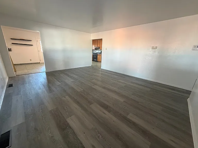 The large living room features new vinyl flooring, that is spacious enough for 3 large sofas, with entry to the backyard. Point of view from the windows, facing the kitchen and dining room entry.