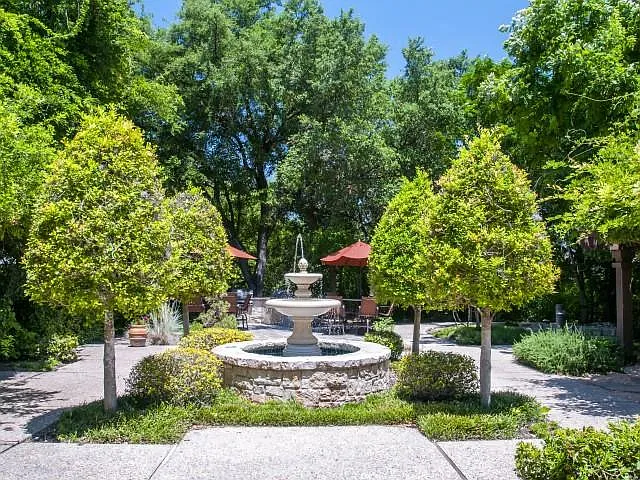 Courtyard water fountain surrounded by sidewalk walking paths and lush greenery