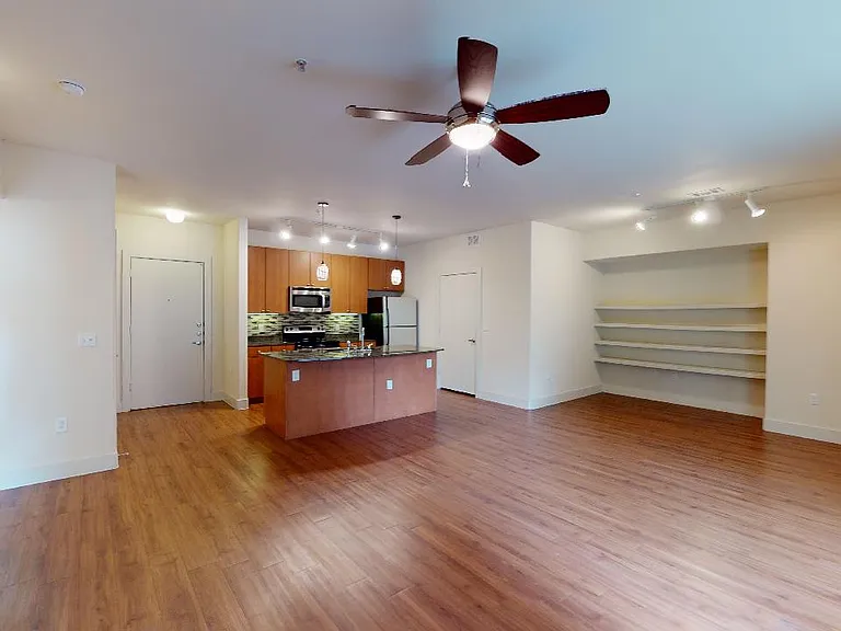 Apartment kitchen with stainless steel appliances, dining and living room with wood-style flooring.