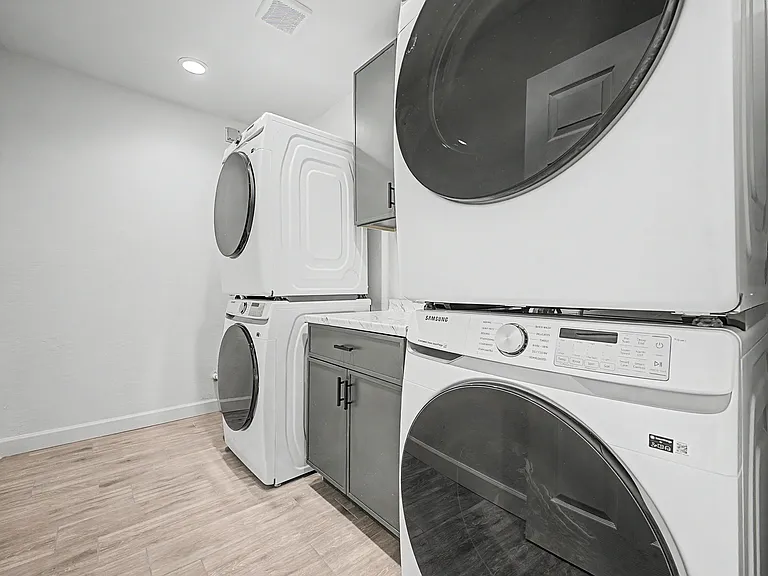Dedicated laundry room with two stacked washer/dryer sets, countertop workspace, and built-in storage cabinetry.