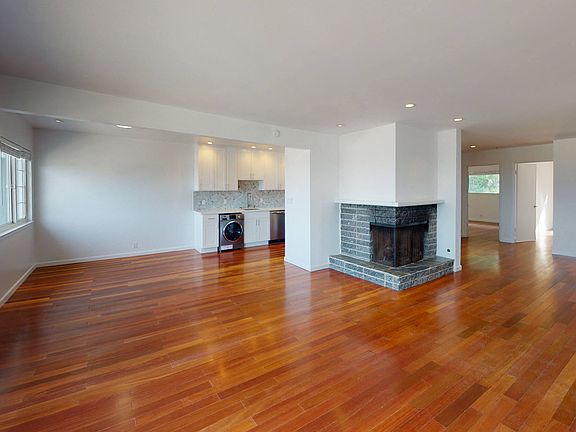 Spacious living area with a fireplace, wood-like flooring and the kitchen at the back