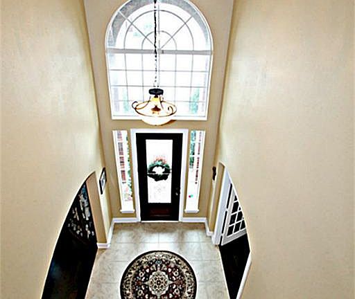 THE SOARING FOYER ILLUMINATED BY A LARGE CHANDELIER SUSPENDED FROM THE SECOND STORY CEILING WITH UPGRADED TILE FLOORS