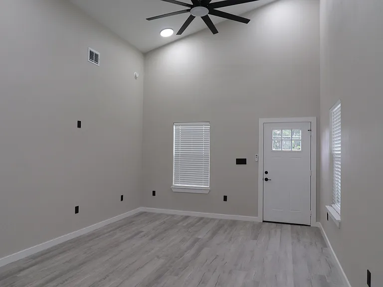 Bright open-concept living area with high ceilings, modern ceiling fan, and abundant natural light. Clean finishes and spacious layout.