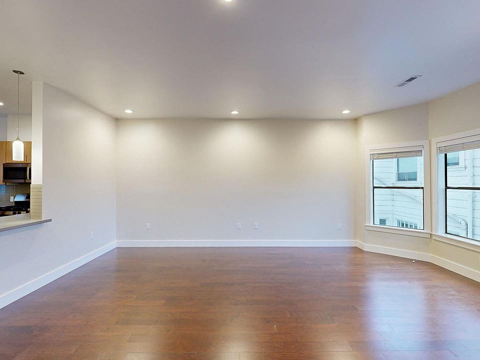 Living room with a large window, wood-like flooring, and entrance to the kitchen