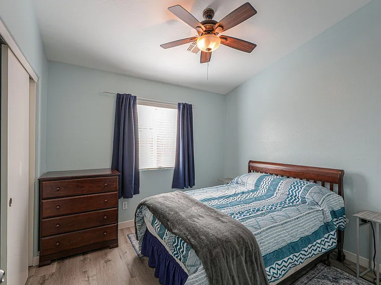 Furnished bedroom with a full bed, dresser storage, window with curtains, and ceiling fan for added comfort.
