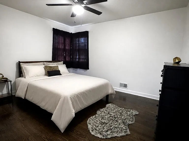 Spacious bedroom with hardwood floors, ceiling fan, and a large window; room for a full bed and dresser storage.