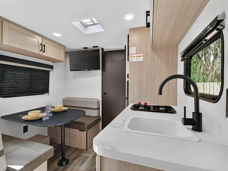 Efficient kitchen with dual-burner cooktop, deep sink, ample cabinetry, and a built-in dinette beside a window.