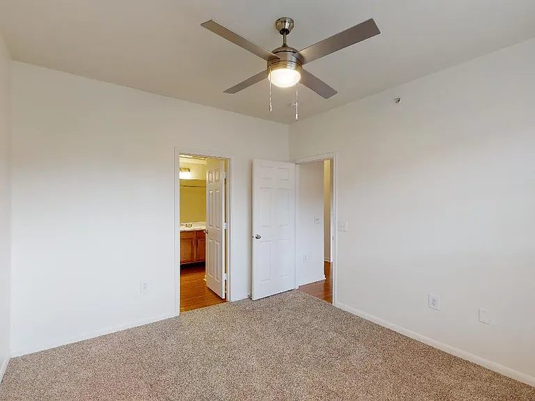 Spacious apartment bedroom with attached bathroom and plush carpet flooring.