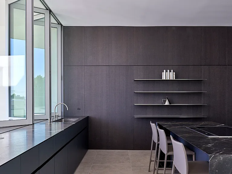 Minimalist Kitchen with Access to Private Terrace _ A refined kitchen featuring floor-to-ceiling dark fumed oak paneling and slender stainless-steel shelves.