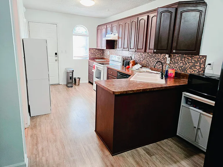 Galley kitchen with ample upper cabinetry, mosaic tile backsplash, and long counters with a breakfast bar and double sink.