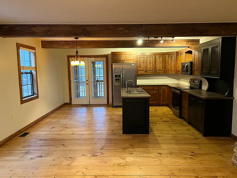 Open concept in living area, custom kitchen and open area behind bar has a furnished dining table.