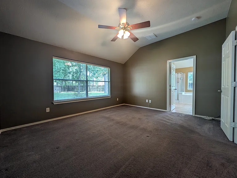 Featuring soaring vaulted ceilings and a ceiling fan, this airy primary suite offers a wide window overlooking the backyard and direct access to the en-suite bathroom.