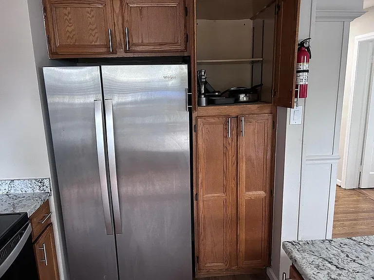 Kitchen features a stainless side-by-side refrigerator, granite countertops, and ample wood cabinetry for storage.