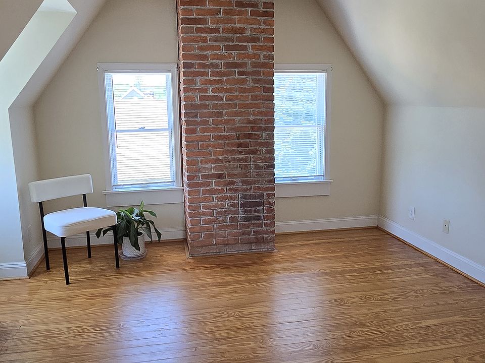 This is the large living space with hardwood floors and an exposed brick chimney. There are 3 large windows and a vaulted ceiling with an exposed beam adding extra drama to the already gorgeous space.