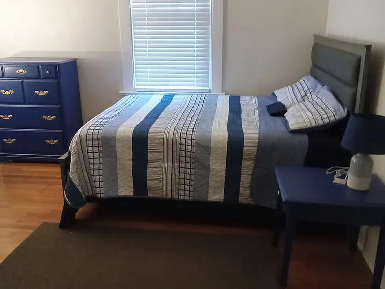 Furnished bedroom featuring a full-size bed, dresser, and nightstand, with a window and hardwood-style flooring.