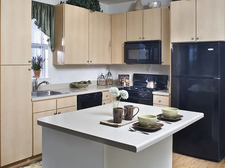 Classic Package I kitchen with light oak cabinetry, beige laminate countertops, white tile backsplash, black appliances, and hard surface flooring