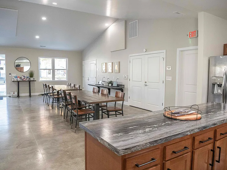 Elegant community room with modern kitchen island, long dining tables, and bright, airy atmosphere.