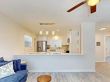 Bright, airy living space with ceiling fan, hardwood-style floors, and seamless kitchen connection