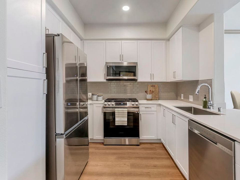 Renovated Package I kitchen with stainless steel appliances, white speckled quartz countertop, white cabinetry, grey tile backsplash, and hard surface flooring