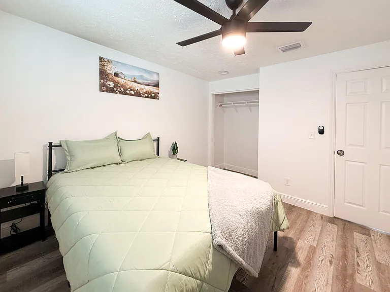 Furnished bedroom with ceiling fan, open closet storage, and nightstand space in a clean, simple layout.