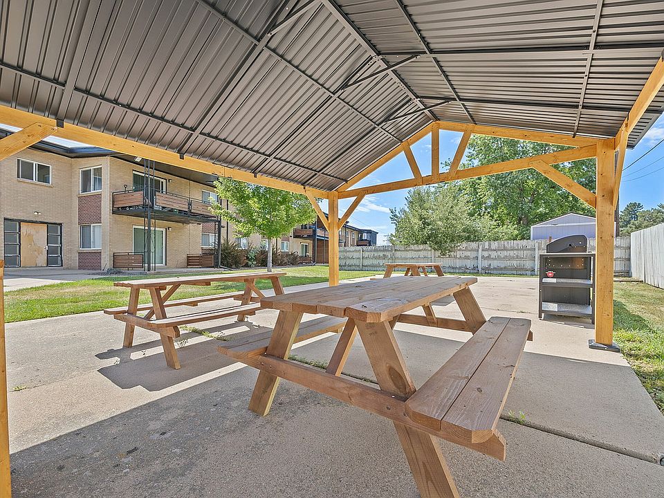Charming outdoor space featuring wooden picnic tables under a cozy gazebo with nearby grill, perfect for gatherings in a serene apartment community.