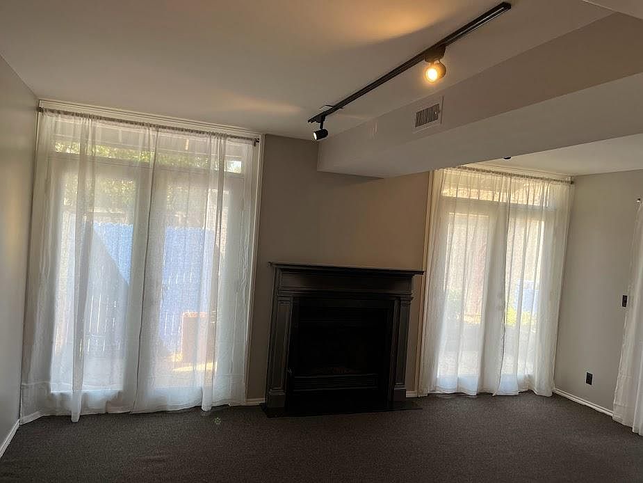 Living room view looking north showing double French doors to patio/garden, gas fireplace, sheer curtains, track lighting.