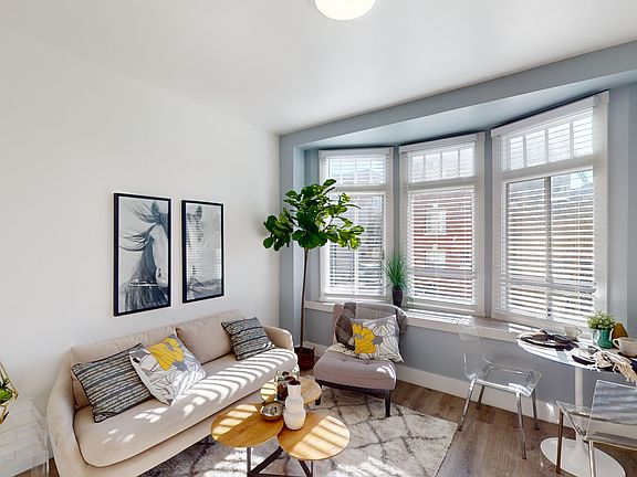 Modern living room with a large window, allowing natural light to flood the space, features a sofa with two throw pillows, armchair, and a wooden coffee table with a vase of flowers