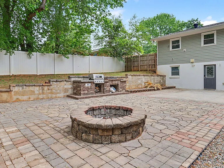 Spacious paved backyard patio with built-in fire pit and outdoor grill area, plus privacy fencing.