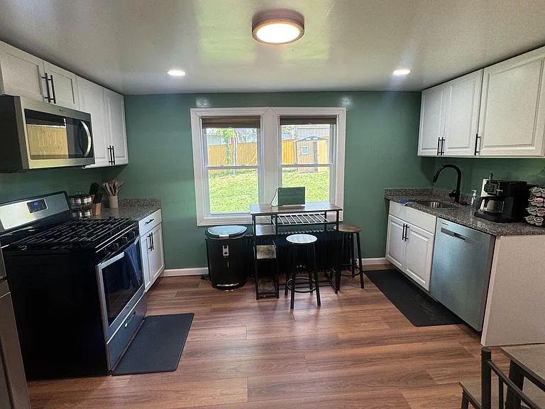 Galley kitchen with ample white cabinetry, stainless appliances, and an eat-in nook by the window overlooking the yard.
