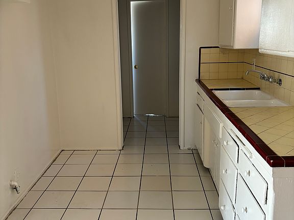 Spacious kitchen with room for a table and chairs on the opposite side.
View is to a little room with additional storage and the bathroom