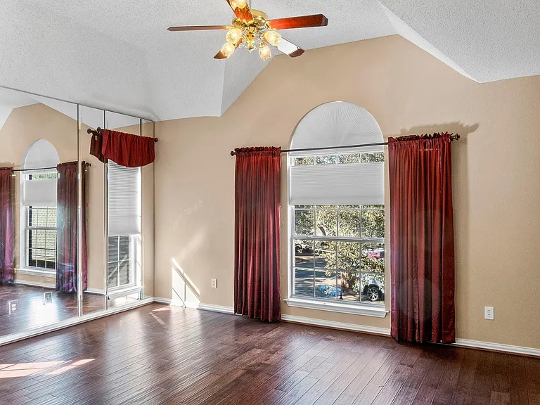 Room featuring wood-finish flooring, vaulted ceiling, and a ceiling fan with light fixture