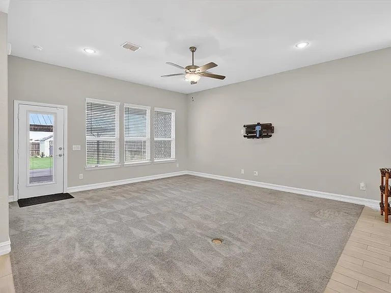 Spacious room featuring neutral carpeting, multiple windows with blinds, a glass-paneled exterior door, a ceiling fan, and recessed lighting